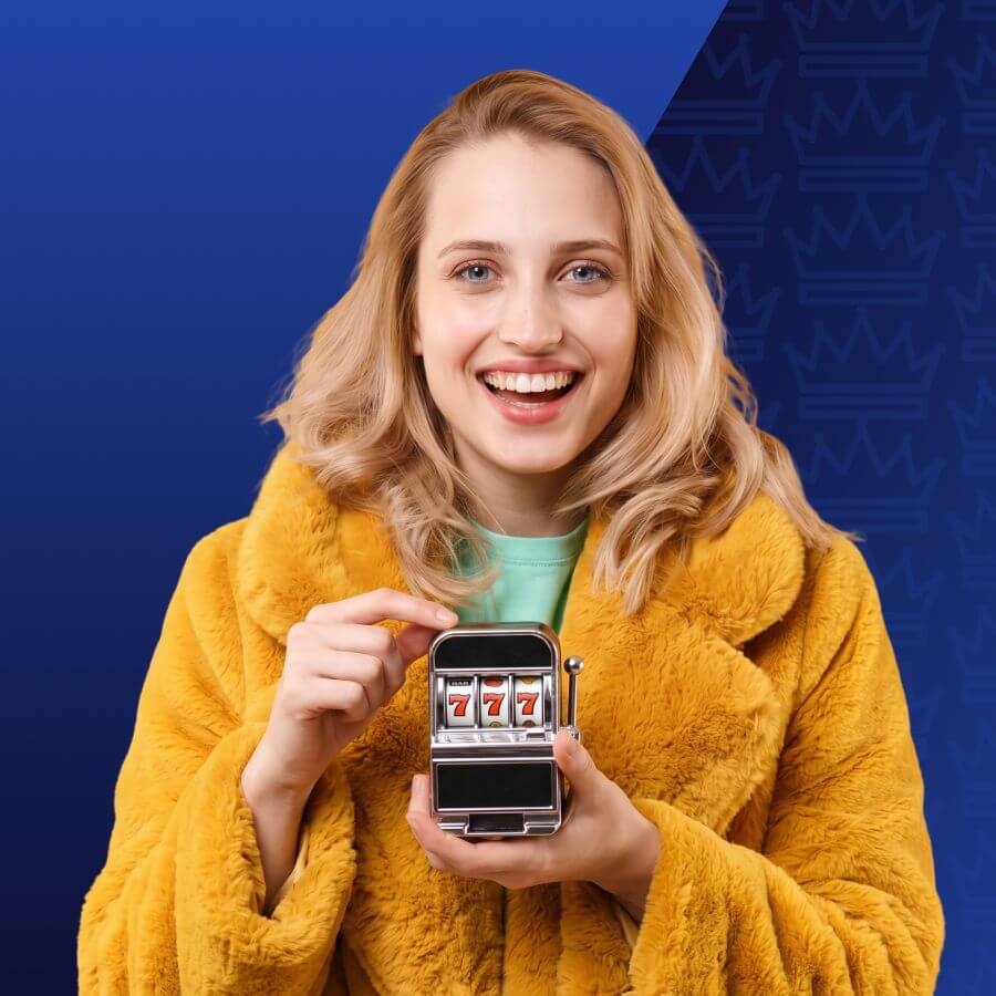 Smiling woman in a yellow faux-fur coat holds a small slot machine showing three sevens against a blue background.